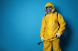 Man wearing protective suit with insecticide sprayer on blue background, space for text. Pest control