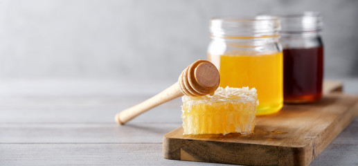 Fresh honey and honeycombs on wooden cutting board. Light floral honey in glass jars