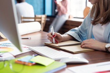 Canvas Print - Young woman working at her desk taking notes. Focus on hand writing on a notepad