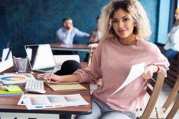 Canvas Print - Portrait of a happy casual businesswoman sitting at her workplace in office