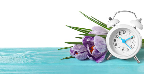Poster - Alarm clock and spring flowers on wooden table against white background, space for text. Time change
