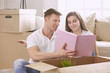 © lenetsnikolai - Portrait of happy couple looking at laptop computer together sitting in new house, surrounded with boxes