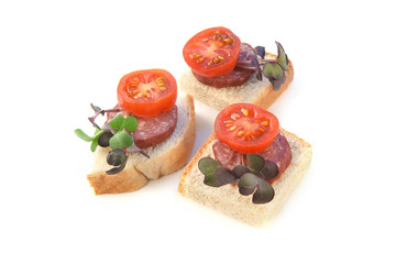 Small sandwiches, finger food, with sliced salami, tomatoes and micro greens radish isolated on white background. Pieces of bread with sausage and vegetables..