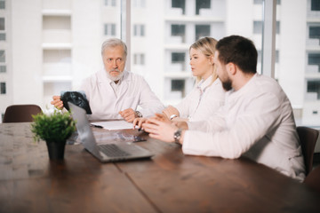 Wall Mural - Medical team of three adult and young doctors examining X-ray scan together in the consulting room of the hospital. View from the doctors' backs, the focus on the X-ray. Concept of team medical work.