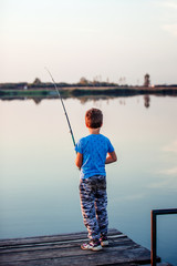 Cute child fishing on a lake in a sunny summer day.