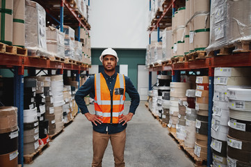 Wall Mural - Manager standing in warehouse between shelf filled with goods wearing a white helmet and orange vest for protection with hands on waist