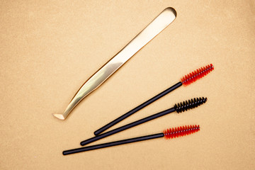  eyelash extension tools, golden tweezers and red-black brushes on a gold background