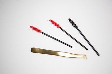  eyelash extension tools, golden tweezers and red-black brushes on a white background