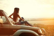 Attractive Yong Woman Is Sitting On The Car's Hood And Looking At Sunset. Rural Evening Background.
