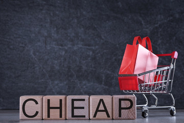 Shopping concept. Wooden cubes with word cheap on dark background with shopping basket