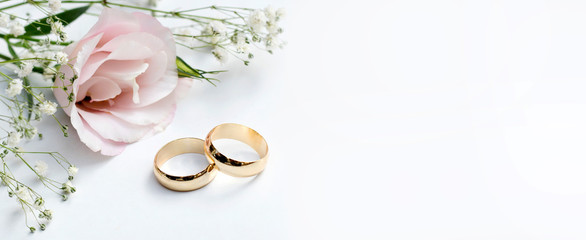 pink flowers and two golden wedding rings on white background.