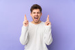 © luismolinero - Caucasian man isolated on purple background with fingers crossing