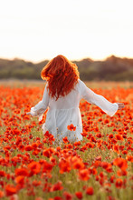 Happy Redhead Smiling Woman In White Dress On Field Of Poppies At Summer Sunset