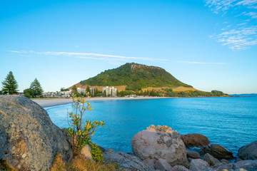 Canvas Print - Mount Maunganui, popular travel and holiday destination with landmark mountain beyong long white beach and rocky foreground.