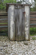An Old Weathered, Wooden Outhouse On Ground Covered With Clamshells.