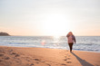 Back view of beautiful overweight woman walking on the sandy beach. Plus size girl enjoy warmth sunset with romantic mood. Fat model dressed jeans jacket and pink knitted sweater