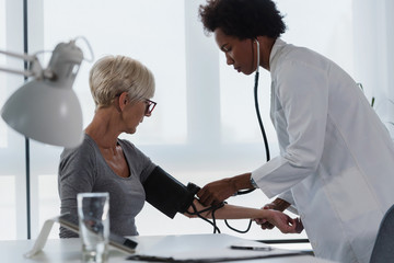 Wall Mural - Female doctor checking blood pressure of a elderly woman at clinic