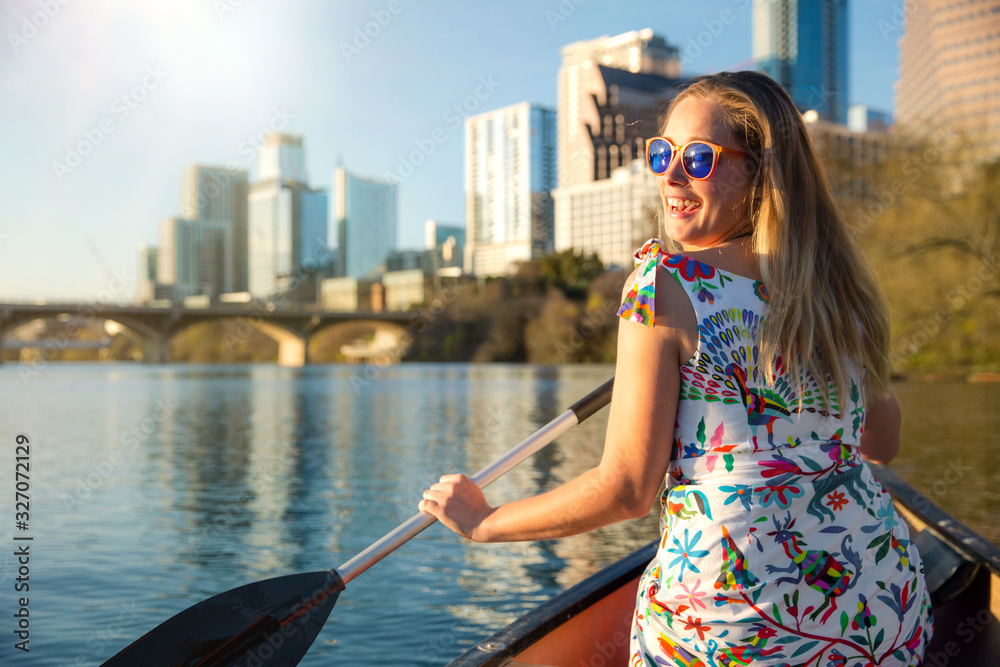 A beautiful traveller enjoying a tourist attraction adventure, kayaking the river near an urban city skyline in the summer - obrazy, fototapety, plakaty 