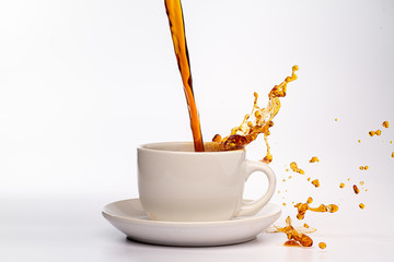 Coffee pouring into a white cup isolated against a plain white background, splashing in all directions creating a mess