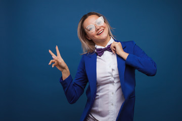 Wall Mural - Funny business lady in a blue jacket and purple bow tie. Jumps for joy and shows a victory sign, two thumbs up.