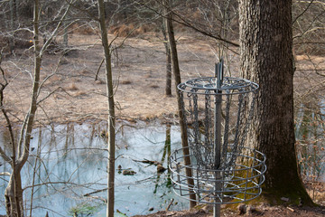 Wall Mural - A Metal Frisbee Golf Chain Hole With a Still River and Trees in the Background