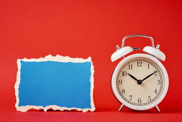 Wall Mural - White vintage classic alarm clock with bells and empty torn paper sheet on the red background.  Design blank for time concept