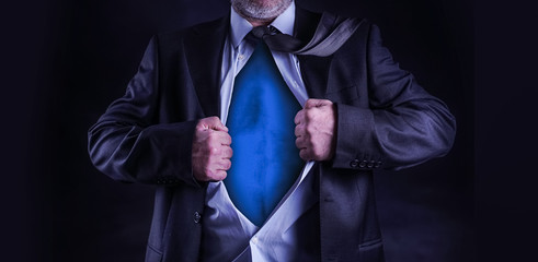 Superhero, young businessman tearing his shirt off isolated on dark background with copy space    