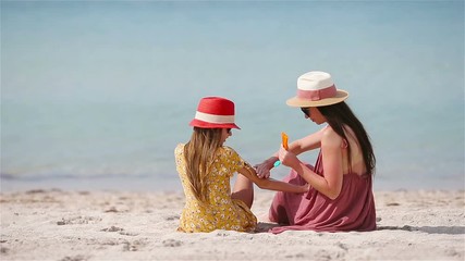 Wall Mural - Young mother applying sun cream to daughter nose on the beach. Sun protection