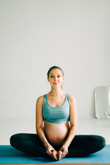 Wall Mural - a young pretty pregnant girl in sports clothes is doing yoga, doing asana Baddha Konasana on the Mat in the Studio