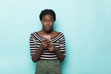 Wall Mural - Beautiful afro woman talking by mobile phone and smiling, standing on blue background.