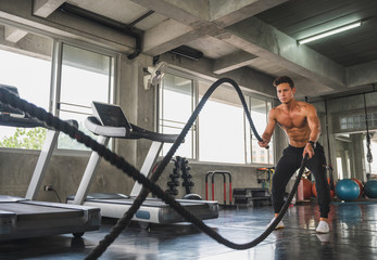 Wall Mural - Young man working out with battle ropes at gym.