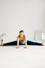 Wall Mural - a young beautiful pregnant girl in sports clothes is doing yoga, performing exercises sitting on a rug in the Studio