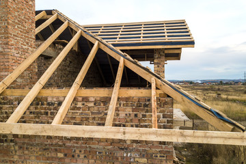 Wall Mural - Private residential house with wooden roof frame structure under construction. Unfinished brick building under development.