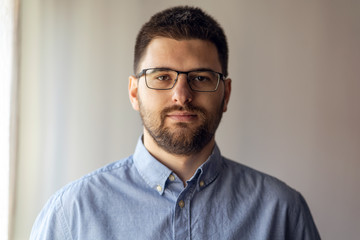 close up portrait of young caucasian man adult wearing shirt and eyeglasses standing by the window f