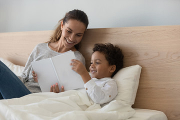 Wall Mural - Smiling mother with African American child reading book in bed