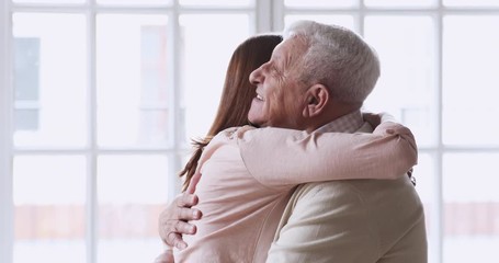 Wall Mural - Happy affectionate young adult granddaughter visit hug senior grandfather