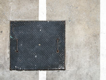 Diamond Metal Plate Manhole Cover On Parking Lot Concrete Floor, Square Black Steel Sheet With Embossed Oval Diagonal Pattern For Closing Drain Sewer And White Dividing Line Of Parking Space, Top View