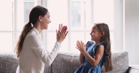 Wall Mural - Female babysitter and kid girl playing patty cake at home