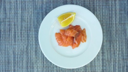 Wall Mural - Salted salmon sliced, and lemon as an appetizing breakfast, top view. The food rotates on a plate, which stands on the table. View from above.