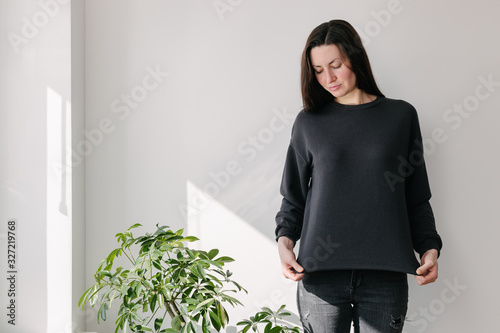 Woman wearing black sweatshirt standing over white wall background. Sweatshirt or hoodie for mock up, logo designs or design prints with with free space