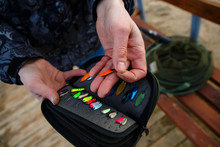 Organizer With A Set Of Artificial Lures For Fishing In The Hands Of A Fisherman. Bright Metal Bait For Catching Trout In A Man's Hand