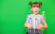 © Svetlana - Photo of confused funny little girl holding plastic bottles and looking at camera isolated over green background