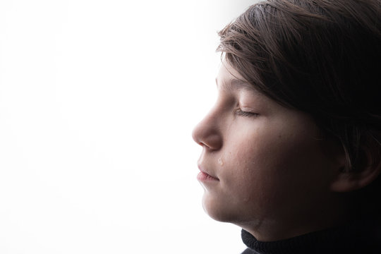 Young sad boy crying with closed eyes. White background. Free space for text. Tear on cheek of unhappy teenager.