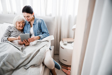 Cheerful old lady and her granddaughter using modern gadget