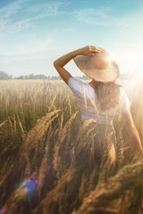 Young woman standing on a wheat field with sunrise on the background