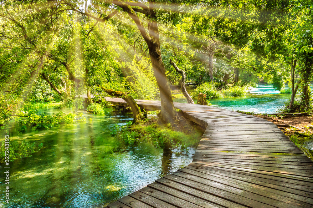 Wooden footpath over river in forest of Krka National Park, Croatia. Beautiful scene with trees, water and sunrays. - obrazy, fototapety, plakaty 