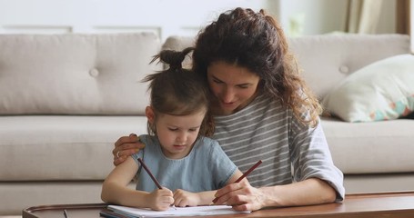 Wall Mural - Affectionate young woman babysitter cuddling small cute kid, drawing together.