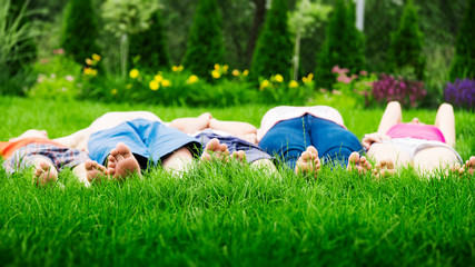 Wall Mural - Family relaxing on green grass, barefoot laying down and looking into the sky