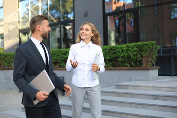 office colleagues talking outdoors near the office building, discussing new project, holding clipboa