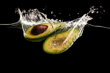 Aufkleber - Avocado halves and water splashes on black background